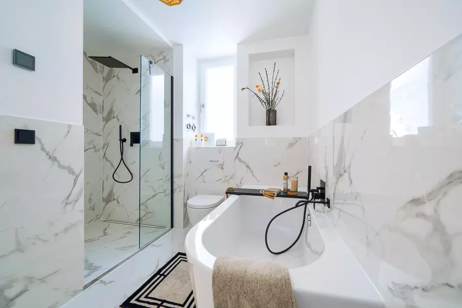Elegantes Badezimmer mit Marmoroptik, schwarzer Armatur und natürlichen Lichtakzenten in einem Münchner Haus, kürzlich saniert.