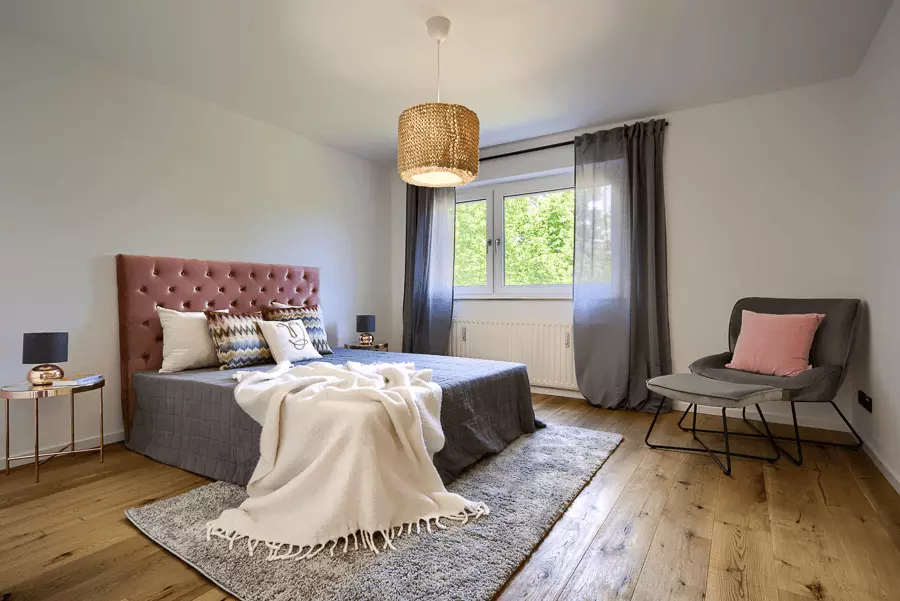 Hell und einladendes Schlafzimmer mit Eichenparkett, rosafarbenem Kopfteil und Blick auf grüne Bäume, frisch renoviert in München.