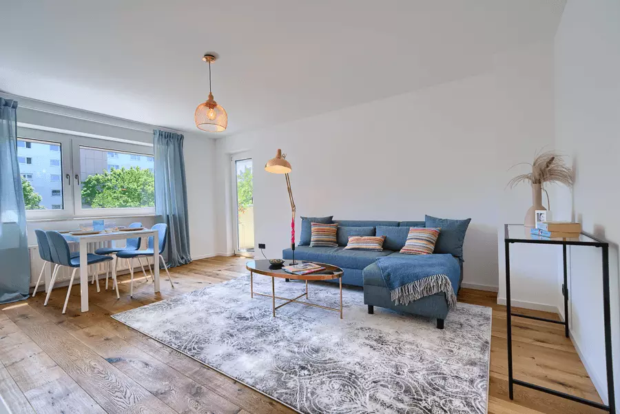 Modernes Wohnzimmer mit blauer Couch, Holzboden und Essplatz, stilvoll renoviert mit viel Tageslicht in München.
