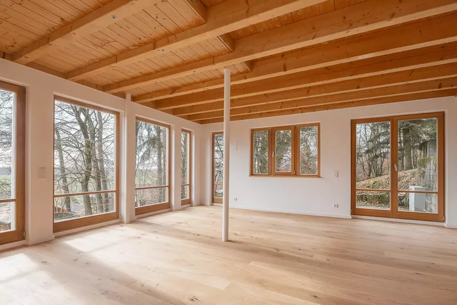 Renoviertes Haus mit Holzbalken, großflächigen Fenstern und Blick auf Bäume, natürliches Wohnambiente