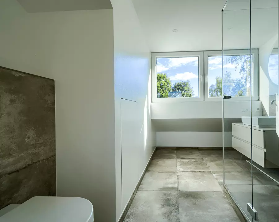 Helles, saniertes Badezimmer mit Betonoptik-Fliesen, gläserner Dusche und minimalistischem Design in München.