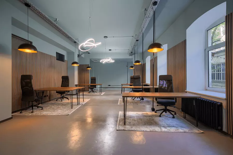 Büro nach Sanierung in München mit Holztischen, schwarzen Stühlen und Industriebeleuchtung, perfekt für modernes Arbeiten.