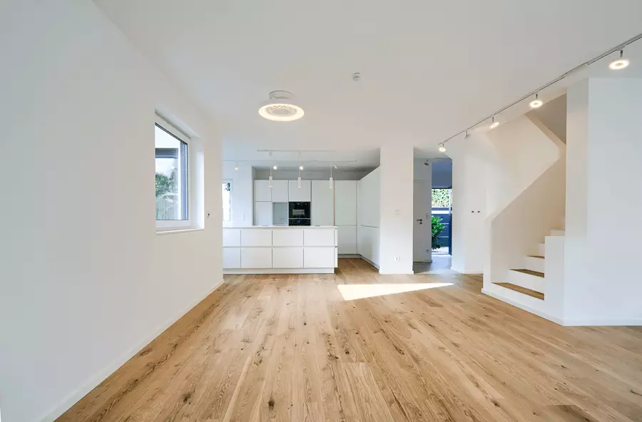 Weiträumiger Wohn- und Kochbereich mit weißer Einbauküche, Eichenholzfußboden und Treppenaufgang, stilvoll saniert in München.