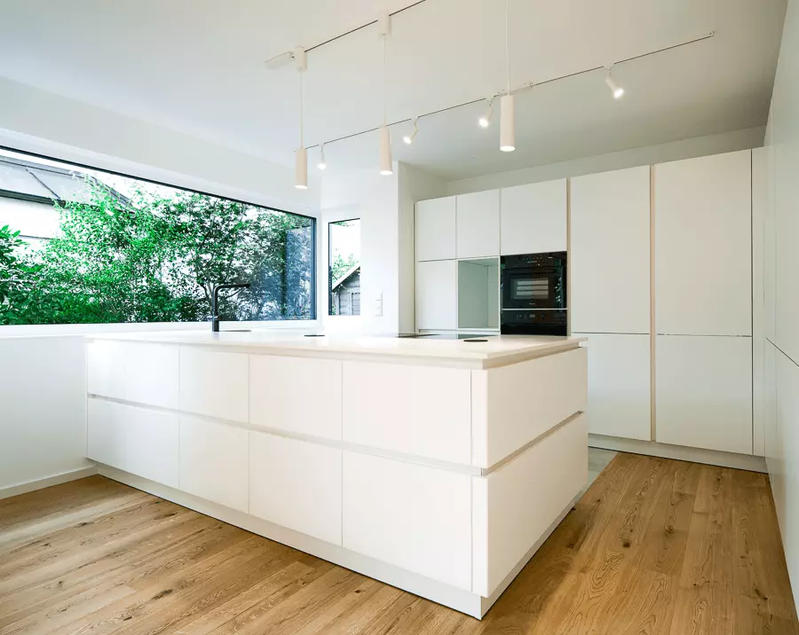 Luftige, helle Küche mit bodenlangen Fenstern, weißen Schränken und Eichenparkettboden, modern saniert in München.